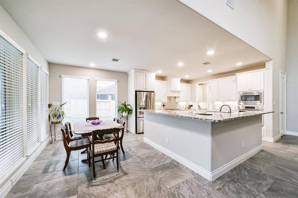This photo showcases a spacious, open-concept kitchen with modern amenities. It features granite countertops, a large island, and stainless steel appliances. The room is bright with ample natural light from multiple windows, and it flows seamlessly into a dining area, making it perfect for entertaining.