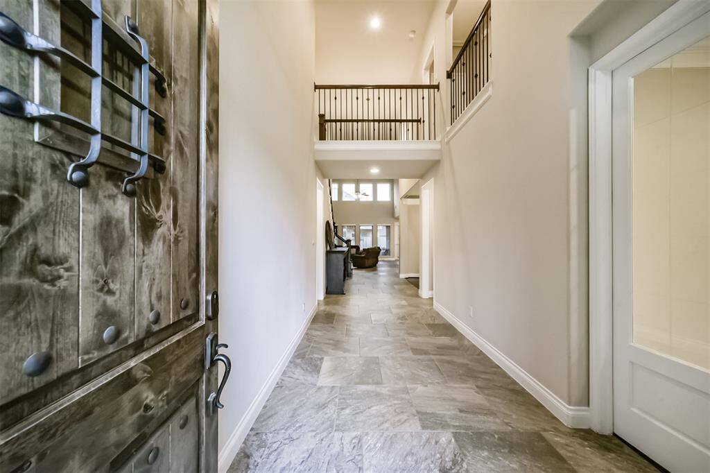 This welcoming entryway features a solid wood door with iron accents, leading to a spacious foyer with high ceilings. The tile flooring adds elegance, and the open layout provides a view into the living area with large windows, offering plenty of natural light.