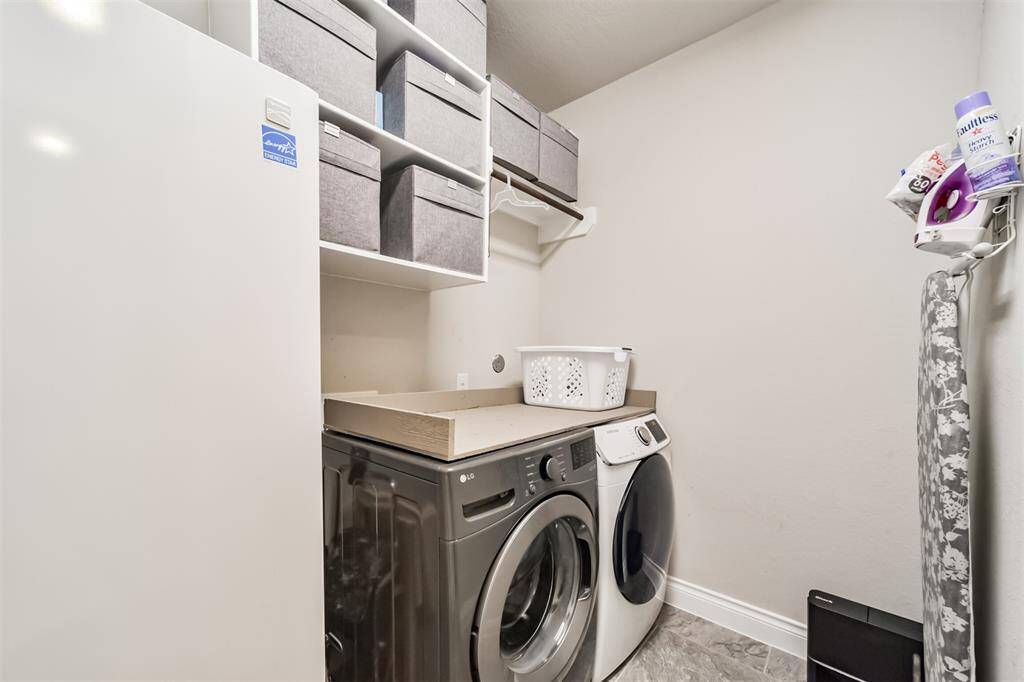 This laundry room is spacious enough for a full sized refrigerator and washer/dryer. Ample shelving with storage bins, and a neat ironing area, offering efficient organization in a compact space.