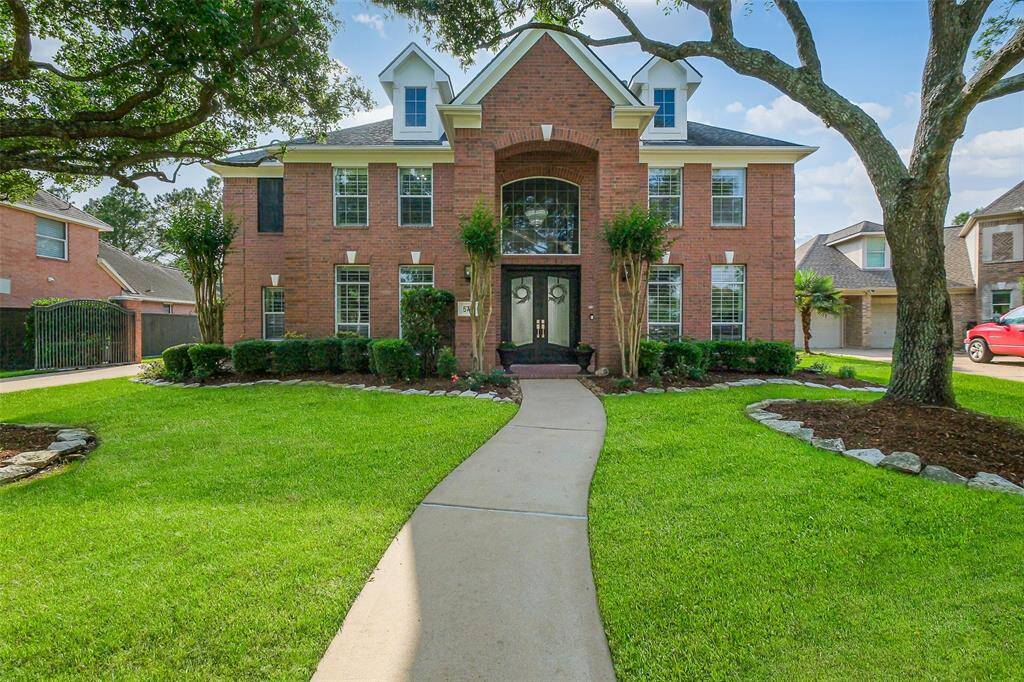 This distinguished two-story brick residence exudes elegance and charm, with its grand façade, arched entryway, and perfectly balanced windows. Rich red brickwork contrasts beautifully with crisp white accents, while lush greenery frames the home, creating a picturesque and inviting presence.