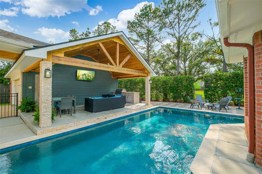 The covered patio, with its tasteful design, offers a perfect view of the sparkling pool in the backyard. Elegant furniture invites relaxation, while the shaded area provides comfort and coolness. Lush greenery surrounds the space, enhancing the serene atmosphere as the gentle sound of water adds a peaceful touch.