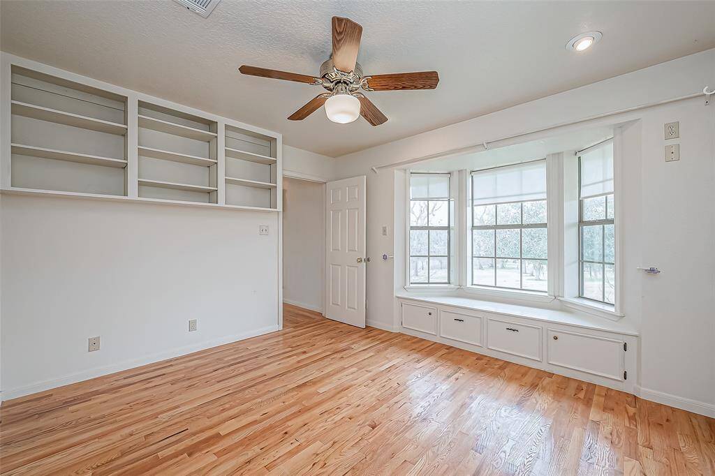 Surrounded by large windows, this bedroom is bright and inviting, with a cozy reading nook nestled beneath the natural light. A built-in overhead shelf offers additional storage without taking up floor space, maximizing the room’s layout.