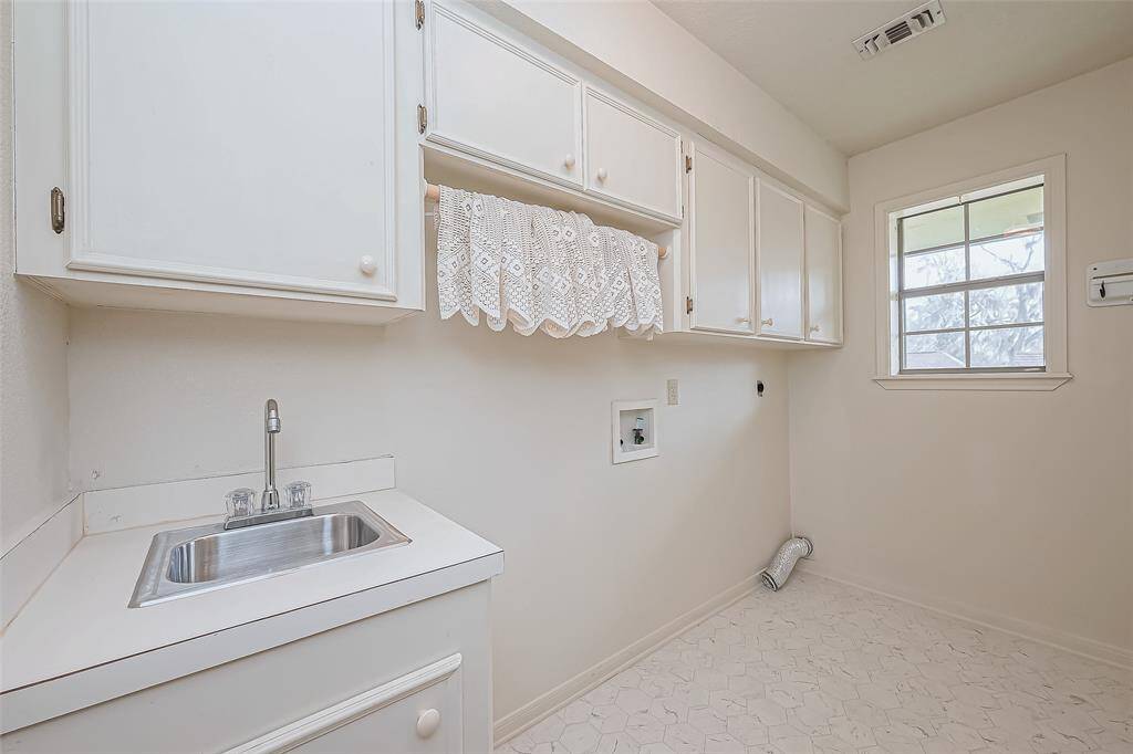 Designed with convenience in mind, this utility room offers ample space for a washer and dryer, with overhead cabinets to keep supplies neatly tucked away. A built-in sink adds extra functionality, perfect for handling laundry or cleanup tasks.