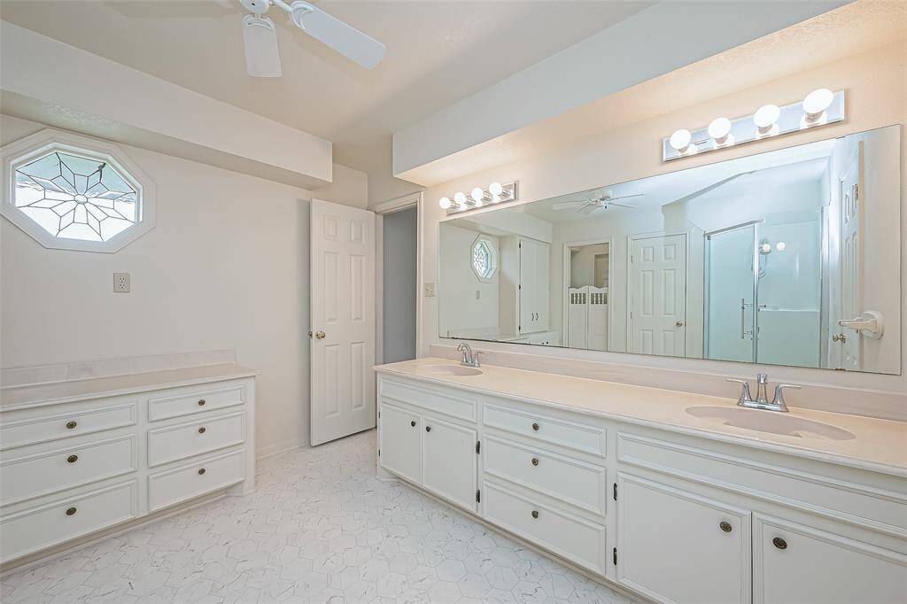 The sleek glass-enclosed shower offers a modern touch, while additional built-in storage near the vanity provides space for essentials. Crisp white finishes create a fresh, timeless look.