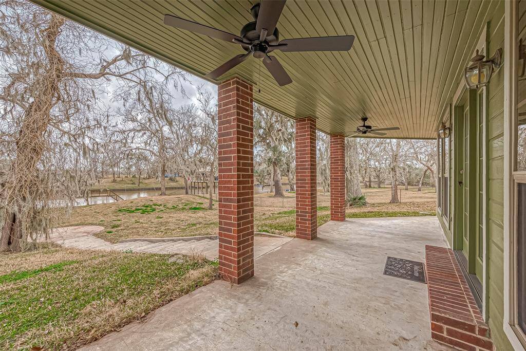 A paved walkway leads from the patio down toward a circular paved area closer to the river, creating an effortless connection between the home and the outdoors. Grass and trees frame the space, blending nature with structure.