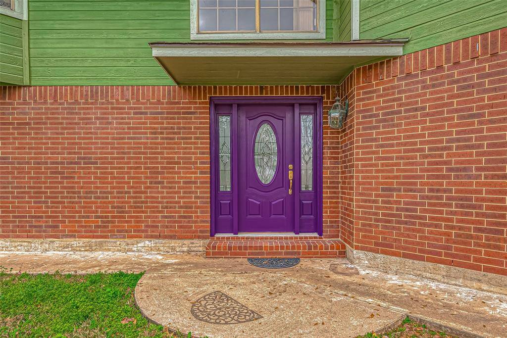 Vivid and full of character, the striking purple door is an unexpected yet delightful contrast to the earthy tones of the home. The covered front entry provides a shaded retreat before stepping inside, offering a perfect spot to add a cozy bench or seasonal décor. From this angle, the craftsmanship of the brickwork and the depth of the architectural details stand out, adding texture and dimension to the home’s facade.
