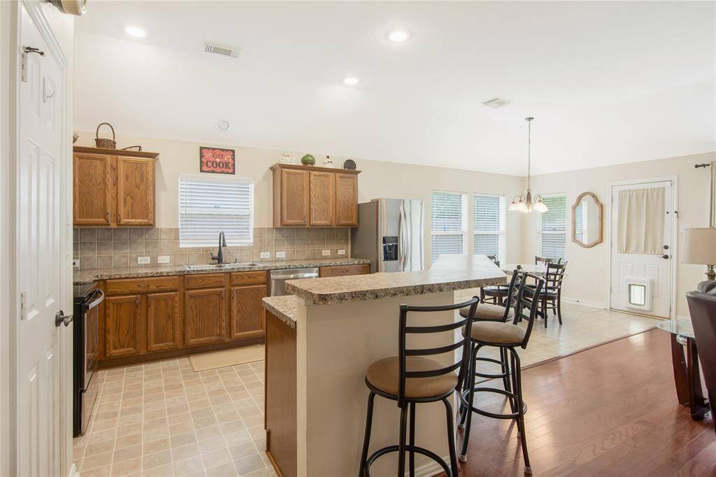 This bright, open kitchen is filled with natural light and features warm wooden cabinetry, a stylish tiled backsplash, and a convenient breakfast bar with seating. It seamlessly flows into a dining area, with a door providing easy access to the outdoors.