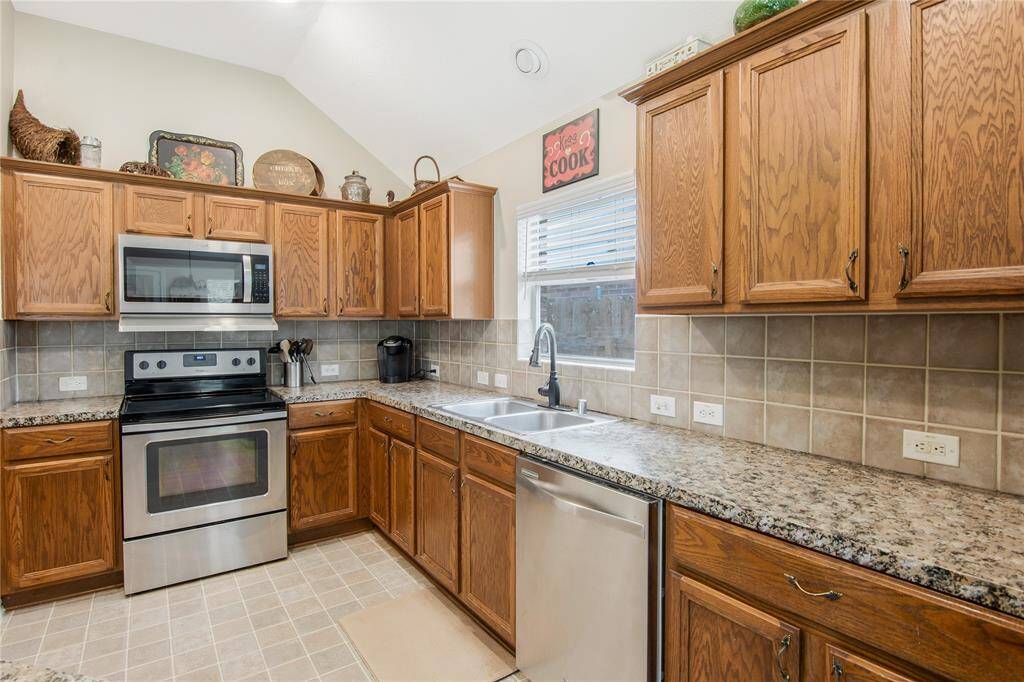 This kitchen features stainless steel appliances, including a built-in microwave and oven, paired with warm wooden cabinets for a modern look. A window above the sink brings in natural light, adding to the bright and inviting atmosphere.