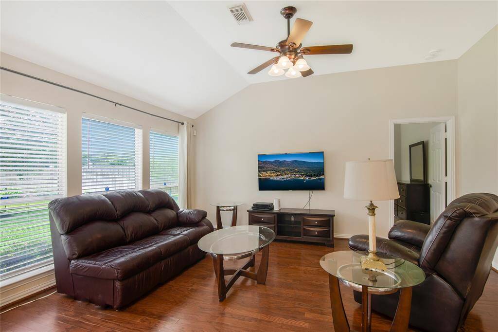 This spacious living room features high ceilings, beautiful hardwood floors, and an abundance of natural light pouring in from large windows, creating an airy and welcoming atmosphere.