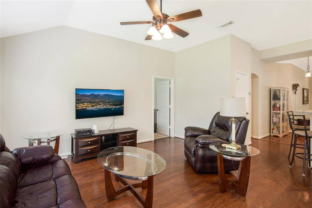 This living room features hardwood floors, neutral walls, and a ceiling fan, creating a cozy and inviting atmosphere. The open layout connects seamlessly to other areas of the home, enhancing the airy, spacious feel.