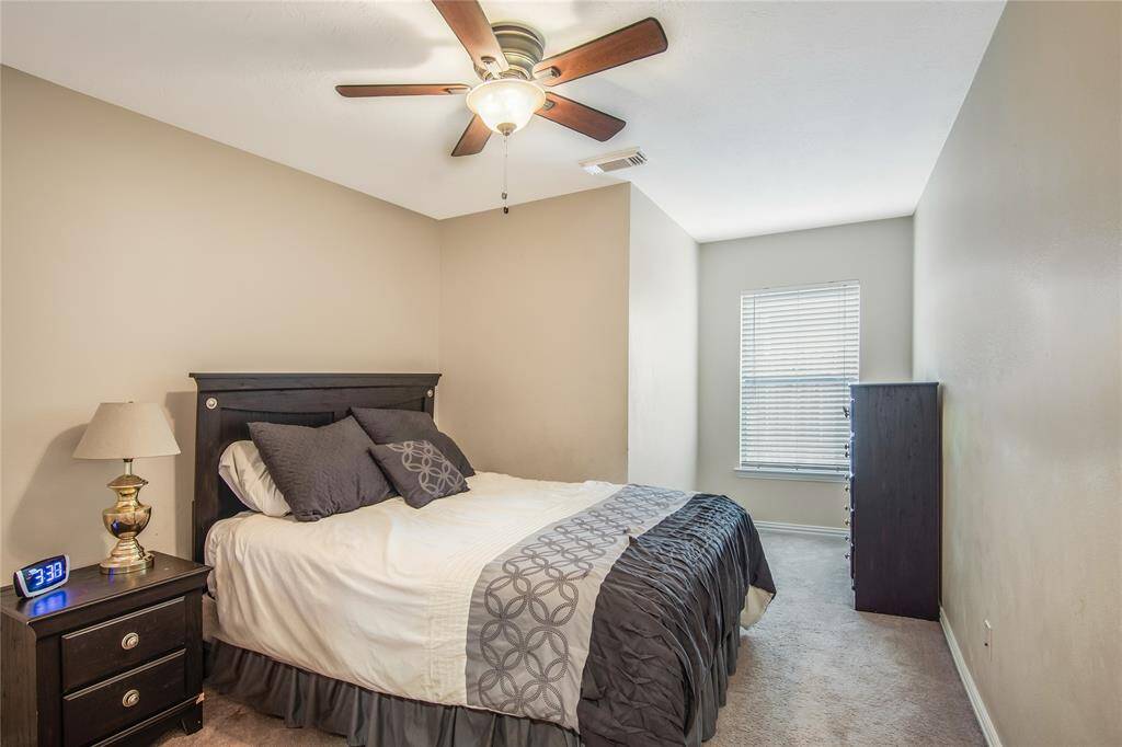This cozy bedroom features a ceiling fan with lighting and a neutral color palette, creating a calm and inviting atmosphere. A window with blinds allows for natural light to fill the space.