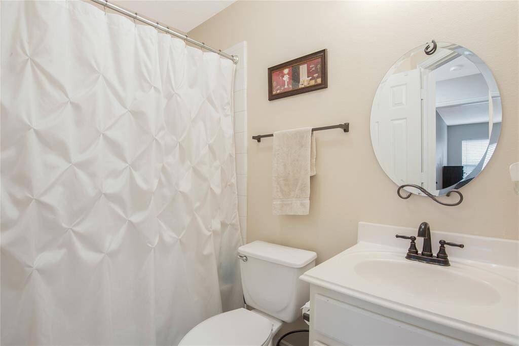 This bright, clean bathroom features a round mirror above the white vanity with sleek dark fixtures, creating a fresh and contemporary look.