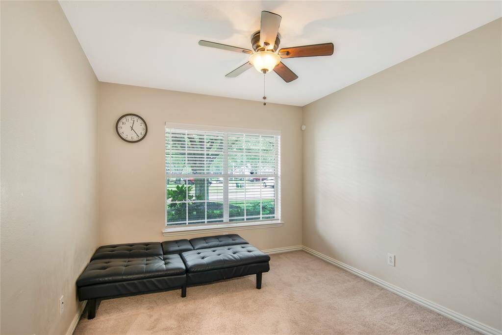 This cozy bedroom features a ceiling fan with lighting, plush carpet, and a window that allows natural light to fill the space.