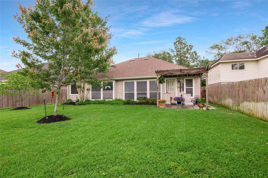 This photo showcases the spacious backyard with a well-maintained lawn, a mature tree, and a wooden fence offering privacy. A small patio with a pergola provides a perfect spot for outdoor seating and relaxation.