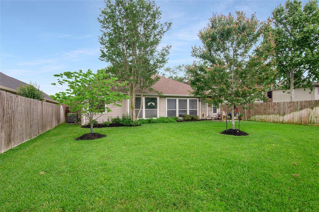 This photo showcases a spacious, well-maintained backyard with lush green grass and a few mature trees. The yard is enclosed by a wooden fence and features a cozy patio area, ideal for outdoor activities and relaxation.