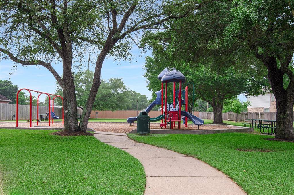 Charming neighborhood playground featuring a colorful play structure and swings, surrounded by lush greenery and mature trees.