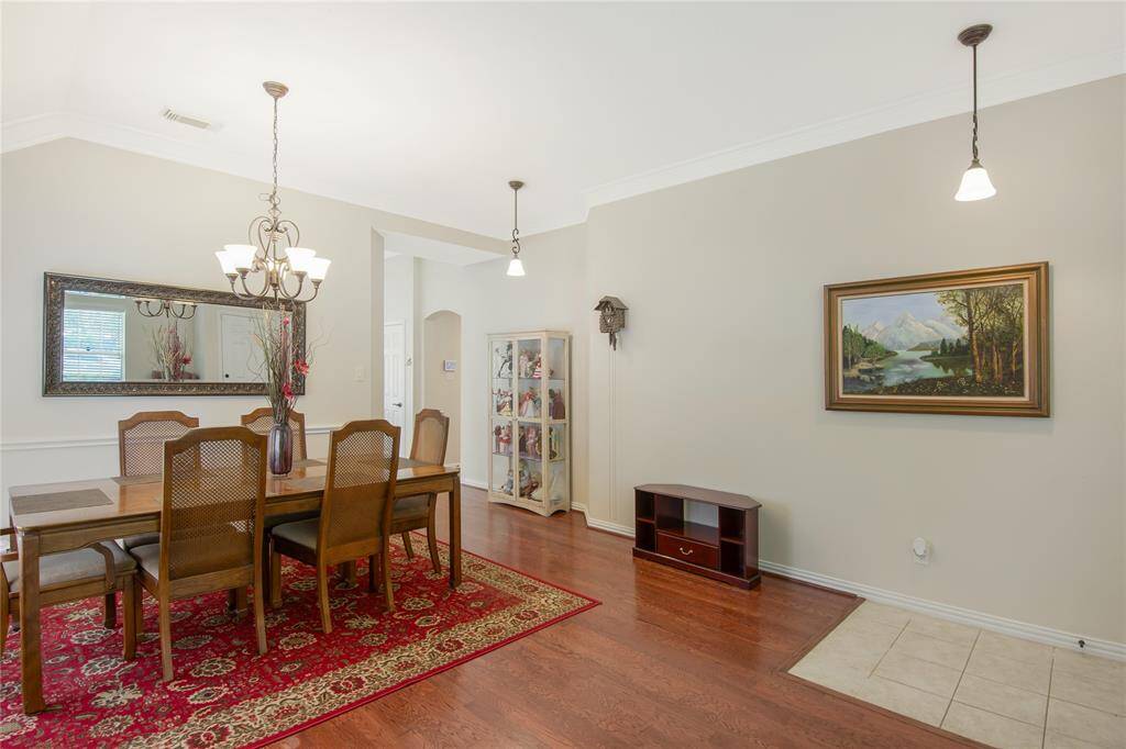 This spacious dining room showcases elegant hardwood flooring and is illuminated by a classic chandelier, adding a touch of sophistication to the space.