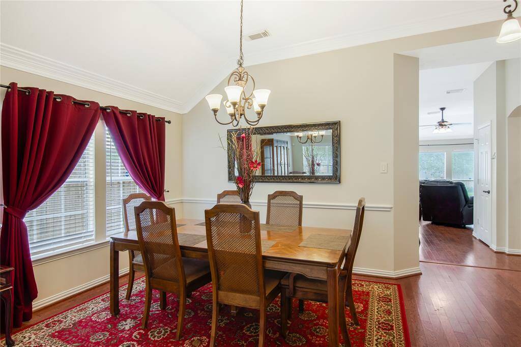 The dining area exudes a warm and inviting atmosphere, highlighted by a classic chandelier, with an open doorway leading into a bright and airy living room.