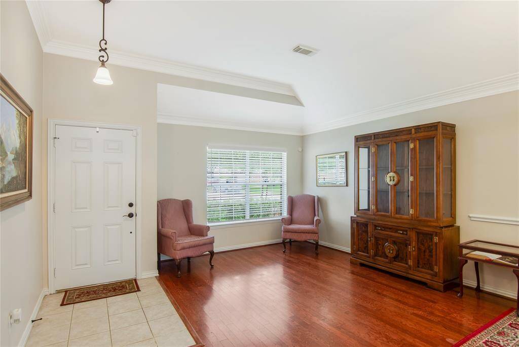 The bright and inviting entryway features gleaming hardwood floors, elegant crown molding, and abundant natural light streaming through a large window, creating a sophisticated and welcoming first impression.