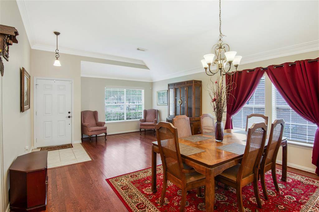 This inviting dining area showcases rich hardwood floors and a striking chandelier, beautifully complemented by large windows that fill the space with natural light. The adjacent sitting area provides a cozy spot to relax and unwind.