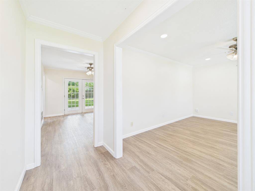Bright, open space with light wood flooring and fresh white walls. Features recessed lighting, ceiling fans, and French doors leading to a garden view. Ideal for seamless indoor-outdoor living.