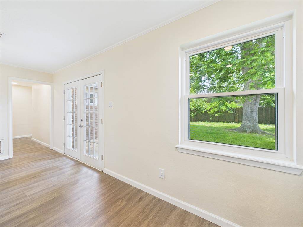 Bright room with large window showcasing a lush green view. The space features freshly painted walls, wood flooring, and elegant French doors leading to the outside.  Cozy and inviting, perfect for enjoying natural light.