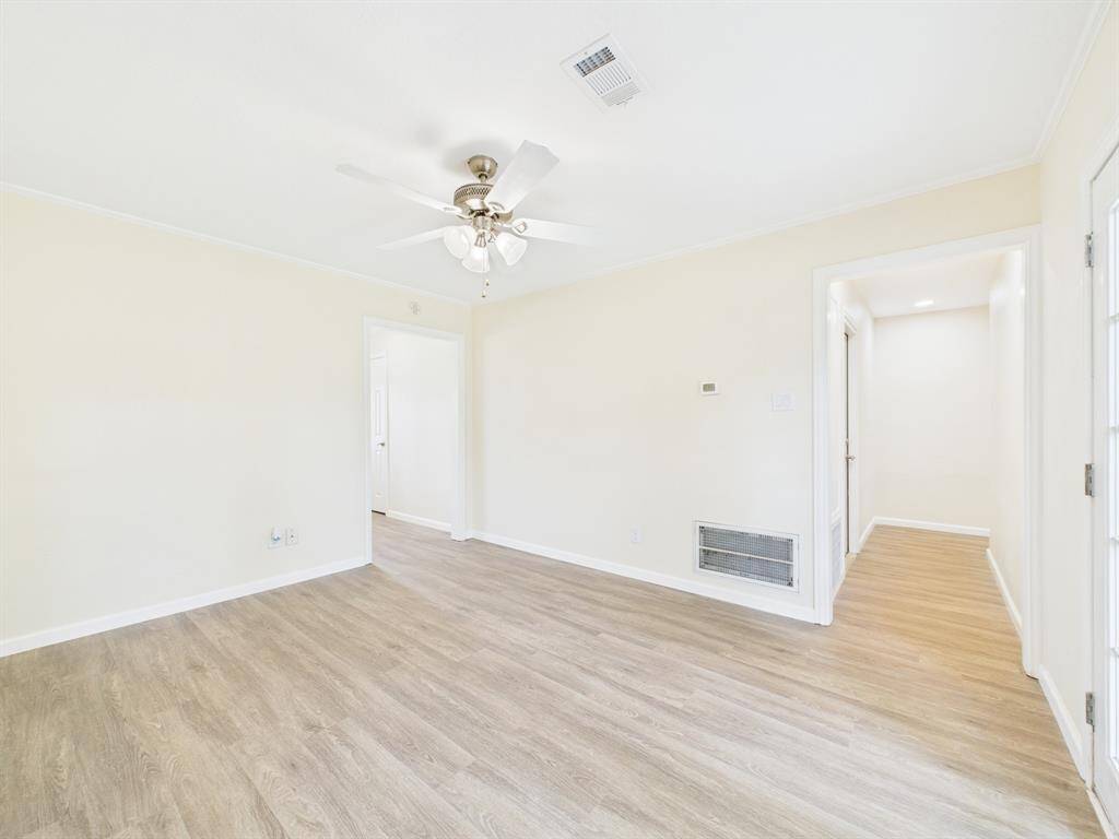 Bright and airy room right off the kitchen with light wood flooring, neutral walls, and a ceiling fan. Perfect for a living or dining space.