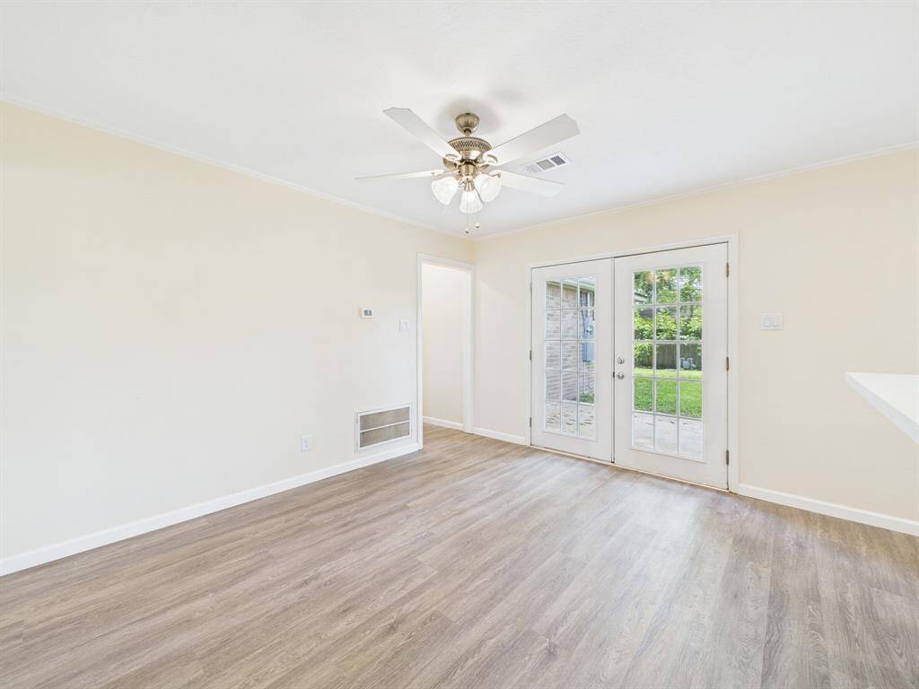 Bright and airy room right off the kitchen with light wood flooring, neutral walls, and a ceiling fan. Perfect for a living or dining space.
