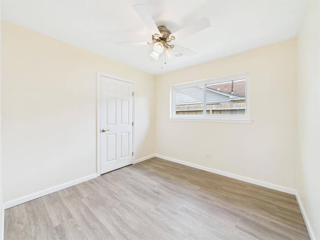 Bedroom #1 is bright and airy with neutral walls and wood-look flooring. It features a ceiling fan and a window providing natural light.