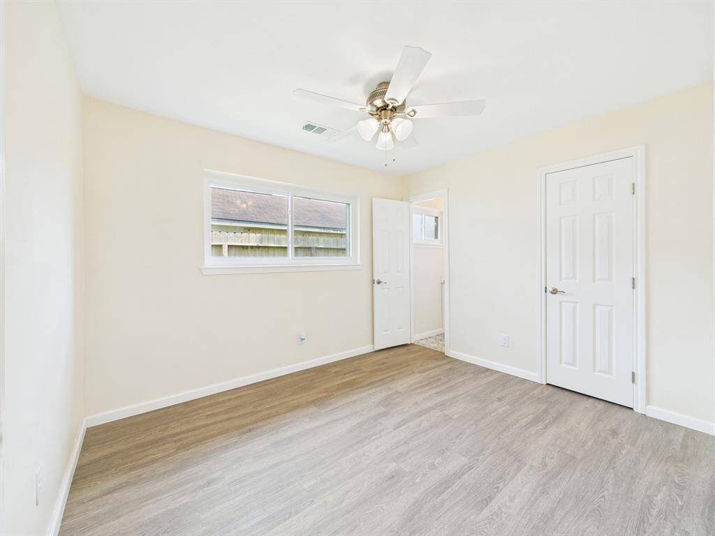 The primary suite features fresh neutral walls, light wood-style flooring, and a ceiling fan. It has a window for natural light, a spacious closet and a 1/2 bathroom for convenience.