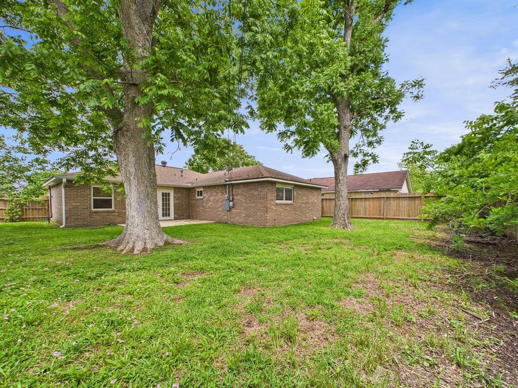 This photo showcases the backyard of a brick house, featuring a spacious grassy area with mature trees and a wooden fence, providing a private and serene outdoor space.