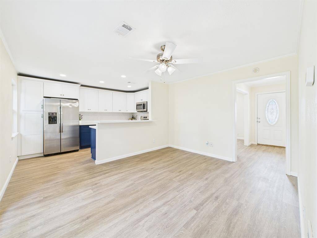 This photo showcases a bright, open-concept living area with light wood flooring. The modern kitchen features stainless steel appliances, white cabinetry, and an island with bar seating. A ceiling fan and recessed lighting add comfort.