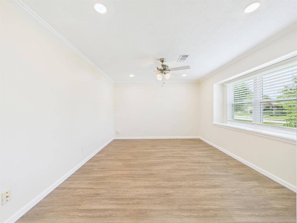 Bright and spacious room with light wood flooring, a ceiling fan, and recessed lighting. Features a large window with blinds, offering plenty of natural light.