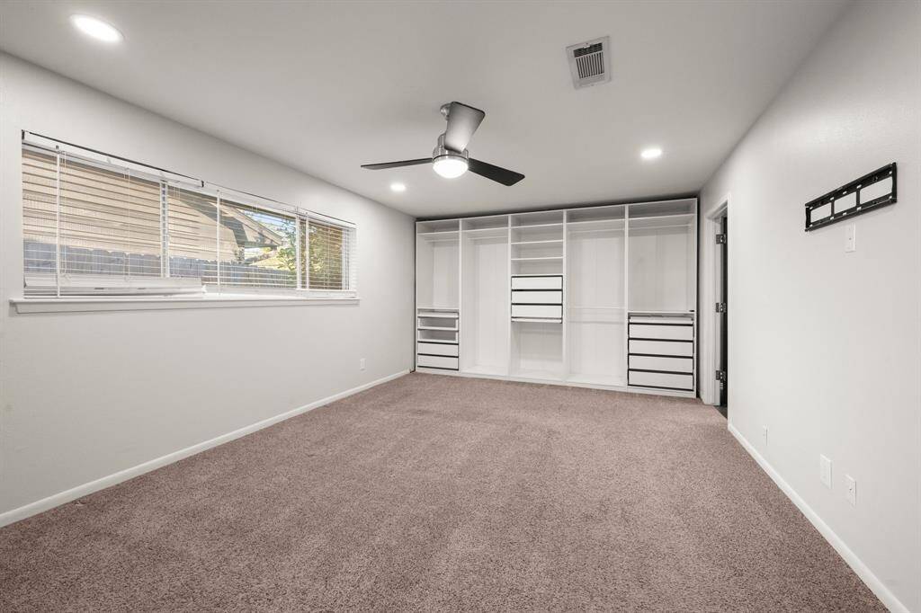Spacious bedroom with a large window, ceiling fan, and built-in closet storage. Neutral carpet and walls enhance natural light, creating a bright and inviting atmosphere.