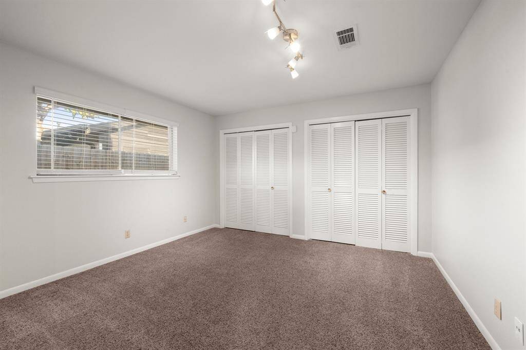 Bright bedroom with neutral walls and carpet, featuring a window for natural light and ample storage with double closets. Ceiling lights add a modern touch.