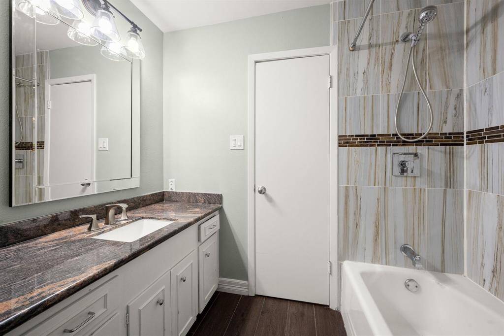 This bathroom features a modern design with a double vanity sink, a large mirror, and elegant countertops. The shower-tub combination has stylish tilework, and the room is well-lit with contemporary fixtures.