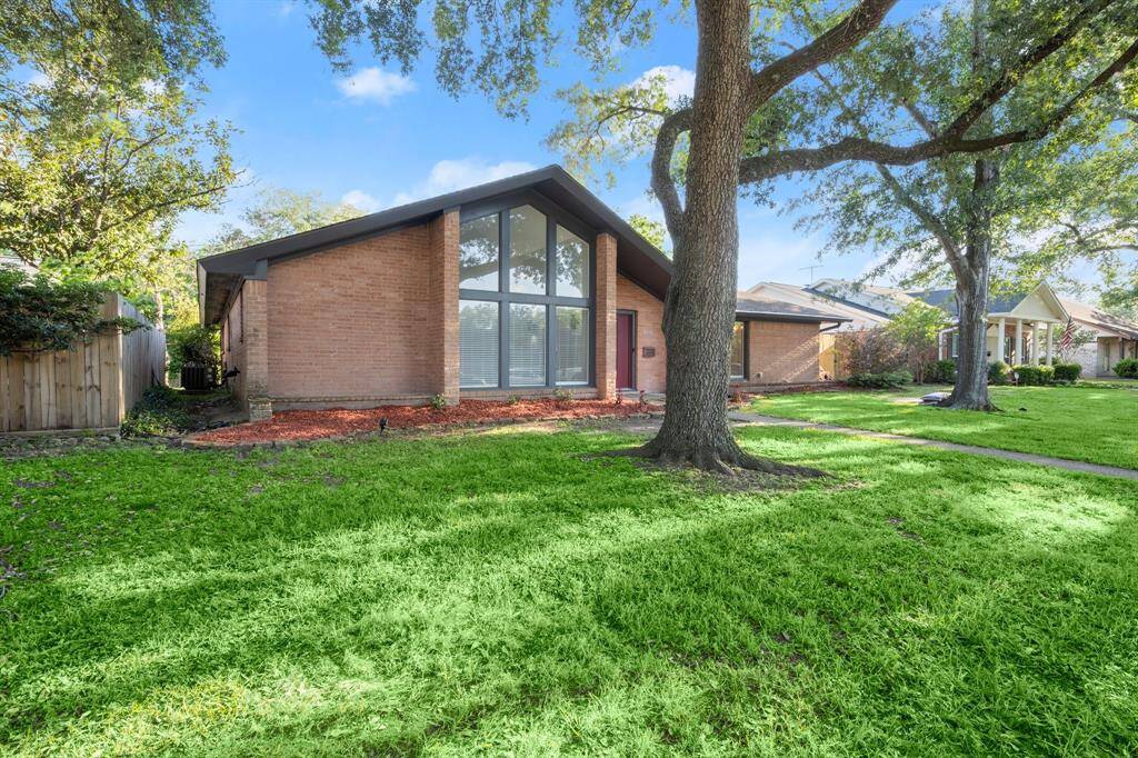 This home features a modern, angular design with large front windows, a brick exterior, and a spacious, tree-shaded front yard. Ideal for those seeking a blend of style and natural surroundings.