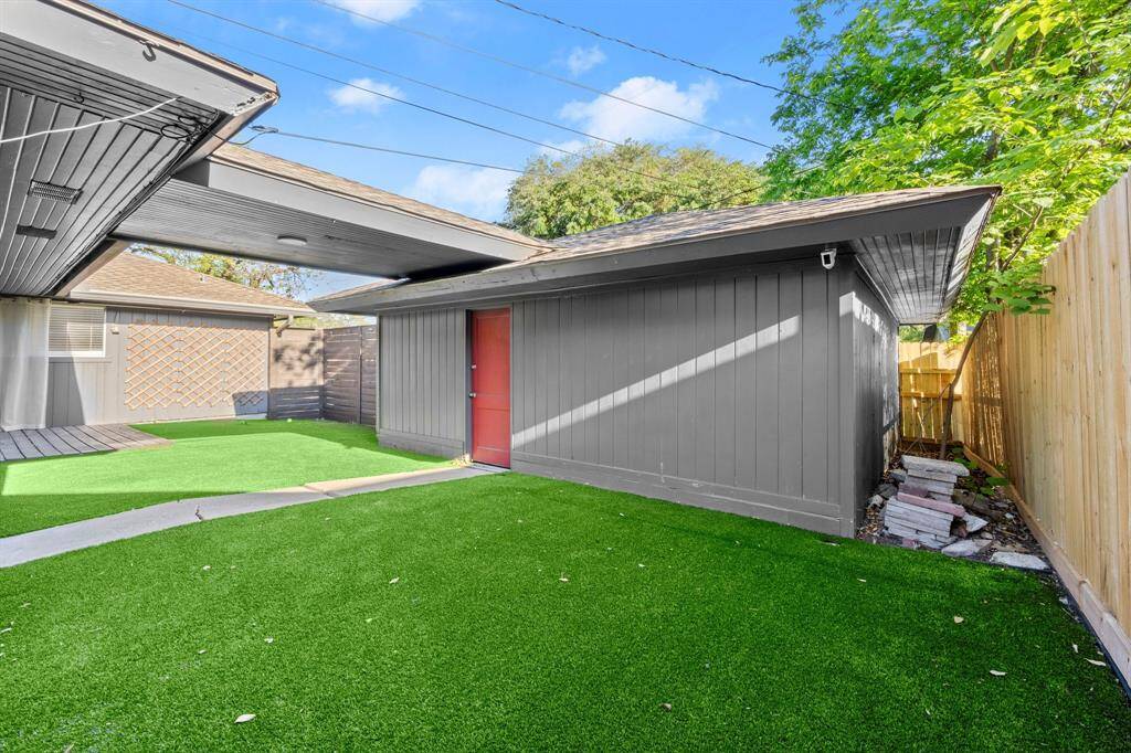This backyard features low-maintenance artificial grass, a modern shed with a striking red door, and a wooden privacy fence, offering a tidy and private outdoor space.