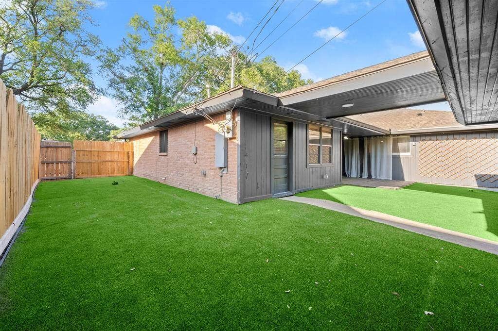 Charming backyard with low-maintenance artificial turf, a wooden privacy fence, and a covered patio area perfect for outdoor relaxation.