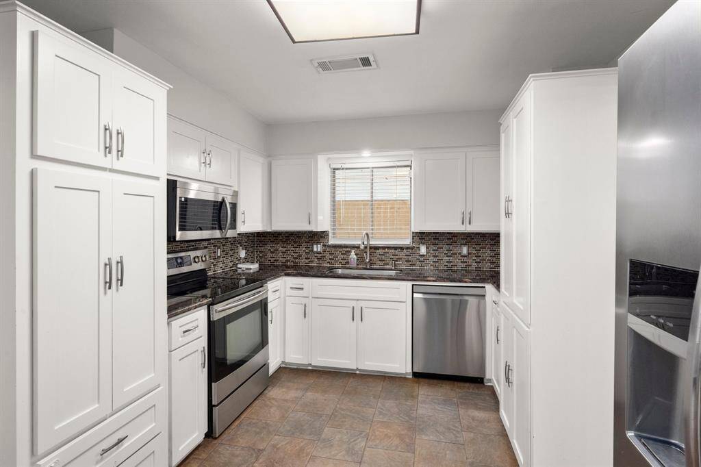 This kitchen features modern stainless steel appliances, sleek white cabinetry, a stylish tile backsplash, and ample natural light, creating a bright and functional cooking space.