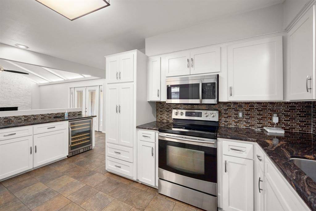 This modern kitchen features sleek white cabinetry, stainless steel appliances, and a stylish mosaic tile backsplash. The space is bright and open, with a wine cooler and ample counter space, perfect for cooking and entertaining.