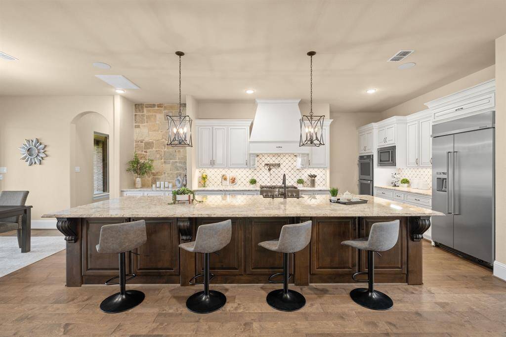 An oversized, contrasting island stands at the center of this stunning chef’s kitchen. It anchors the space with convenient bar seating, a deep basin farmhouse sink, and eye-catching pendant lights above. The open-concept layout blends style and function, offering seamless connection to the casual dining area and family room, making it perfect for both entertaining and everyday living.