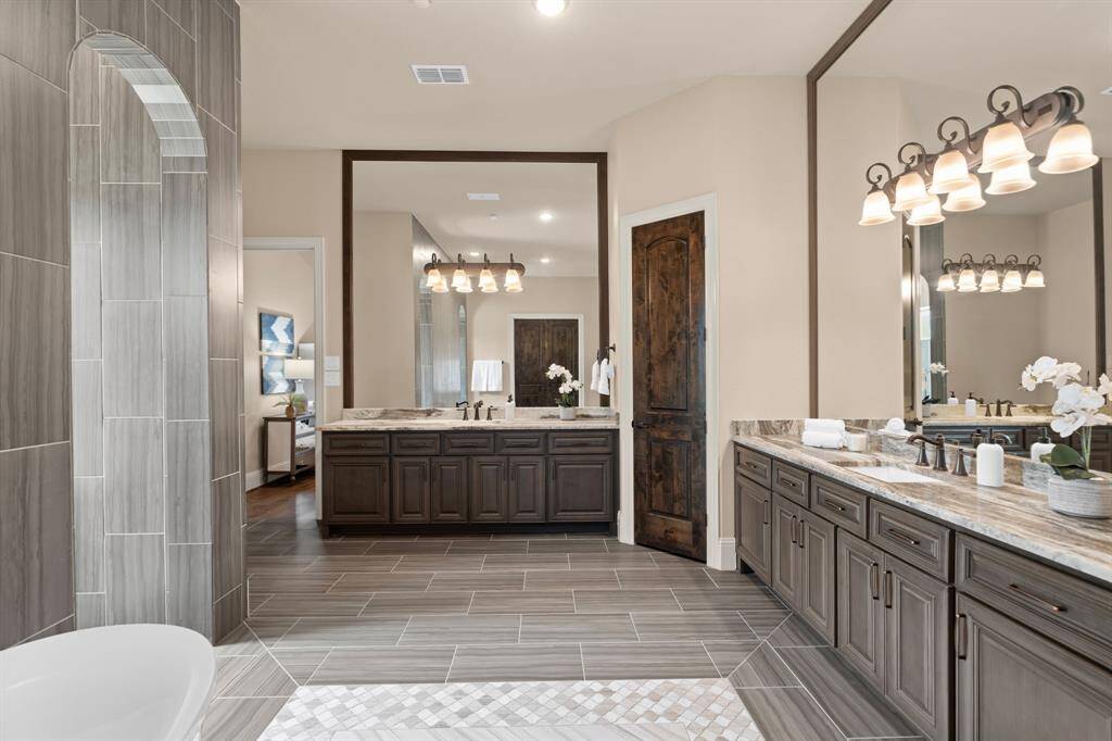 The owner’s ensuite bathroom exudes luxury, featuring separate granite vanities with full-framed mirrors and integrated in-mirror lighting. The expansive Greek shower and the luxurious free-standing soaking tub create an ideal space for relaxation, offering a spa-like retreat where every detail enhances comfort and indulgence.
