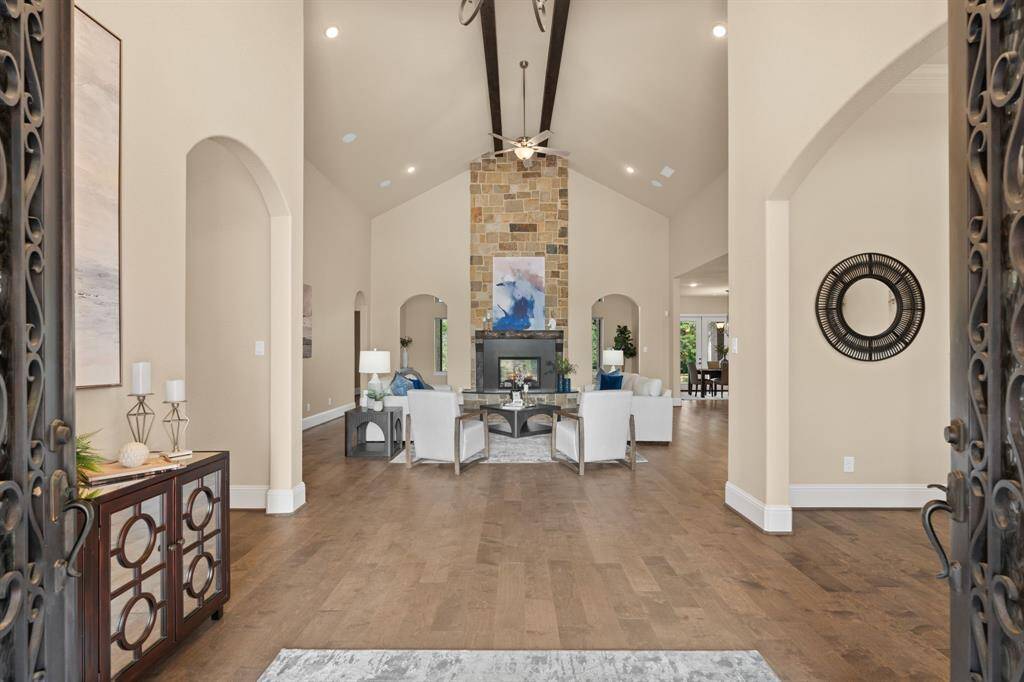 It will be love at first sight! Step through the elegant wrought-iron doors and into a breathtaking living space where a soaring cathedral ceiling with exposed wood beams draws the eye upward, while rich engineered wood flooring grounds the space with timeless elegance. At the center, a stunning two-sided stone fireplace serves as both a striking statement piece and a cozy gathering spot, setting the tone for the luxury and thoughtful design that defines this exceptional home.