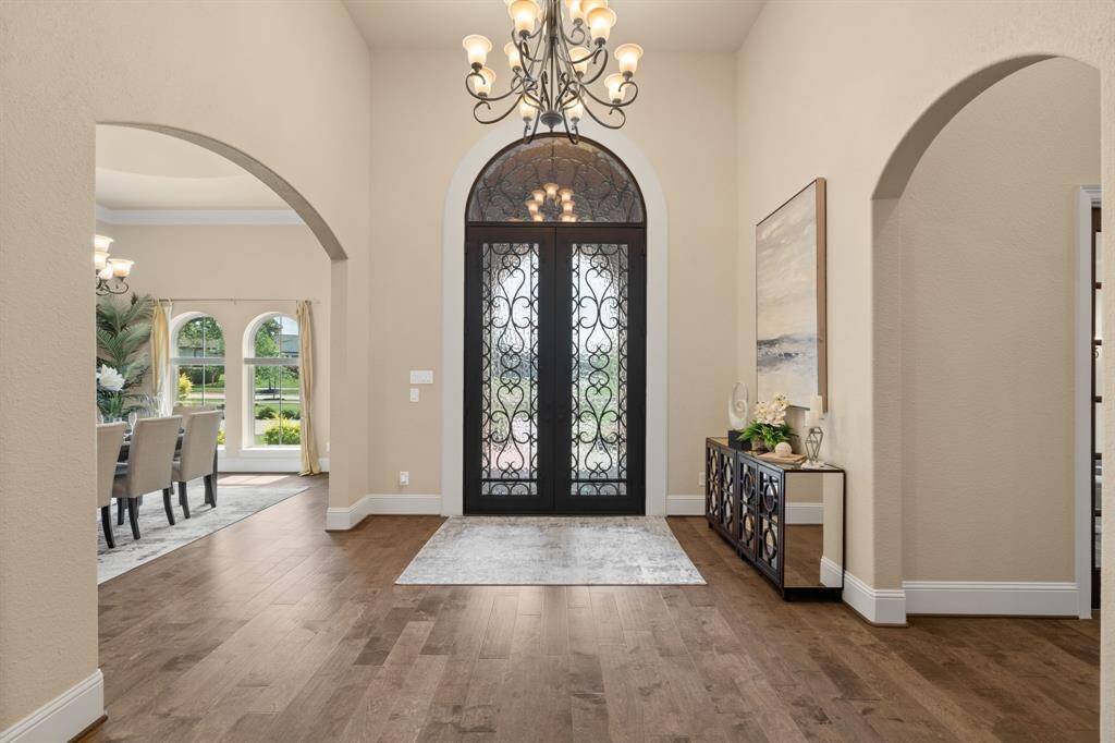 Welcome to elevated living, where elegant wrought-iron double doors open to a grand entry with a soaring 15’ ceiling and a dazzling chandelier, setting the stage for refined style and luxurious finishes.