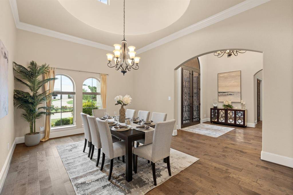 Designed to impress, the formal dining room sits beneath a soaring rotunda ceiling with a grand chandelier and arched windows that frame peaceful front yard views. Elegant crown molding, warm engineered wood flooring, and easy access to the chef’s kitchen make this the perfect setting for unforgettable gatherings and everyday elegance.