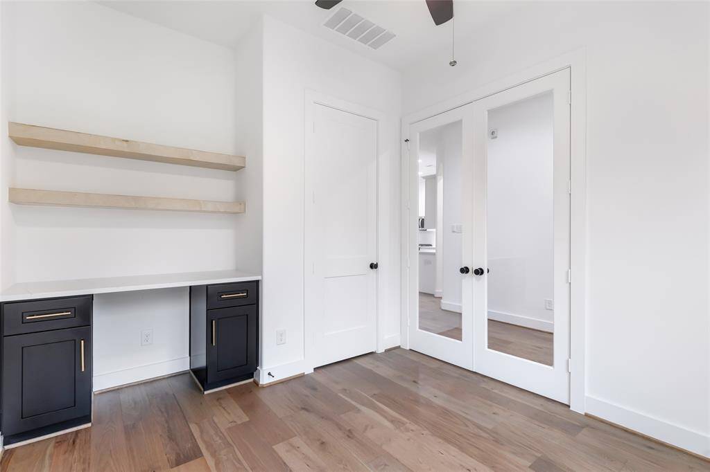 This is a bright, modern room featuring wooden floors, built-in shelving, and a sleek desk with black cabinets. It has double glass doors and a closet and can be used as a 4th bedroom