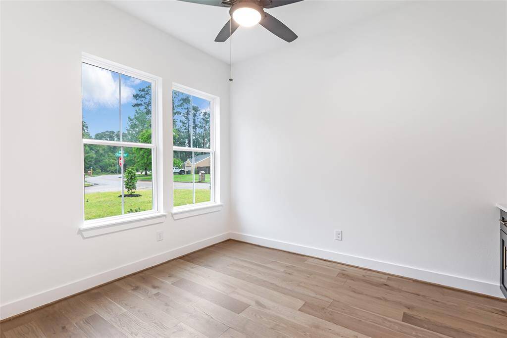 This bright room features large windows with a view of greenery, sleek hardwood floors, and a ceiling fan, offering a cozy and inviting space.