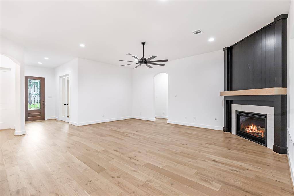 This spacious living room features elegant hardwood floors, a cozy fireplace with a modern black surround, and ample natural light. It also includes a stylish ceiling fan