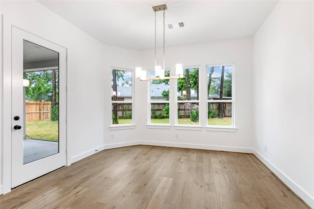 This bright dining area features large windows with a view of the backyard, hardwood floors, and a modern chandelier. A glass door provides easy access to the outdoor space, enhancing natural light and connectivity.